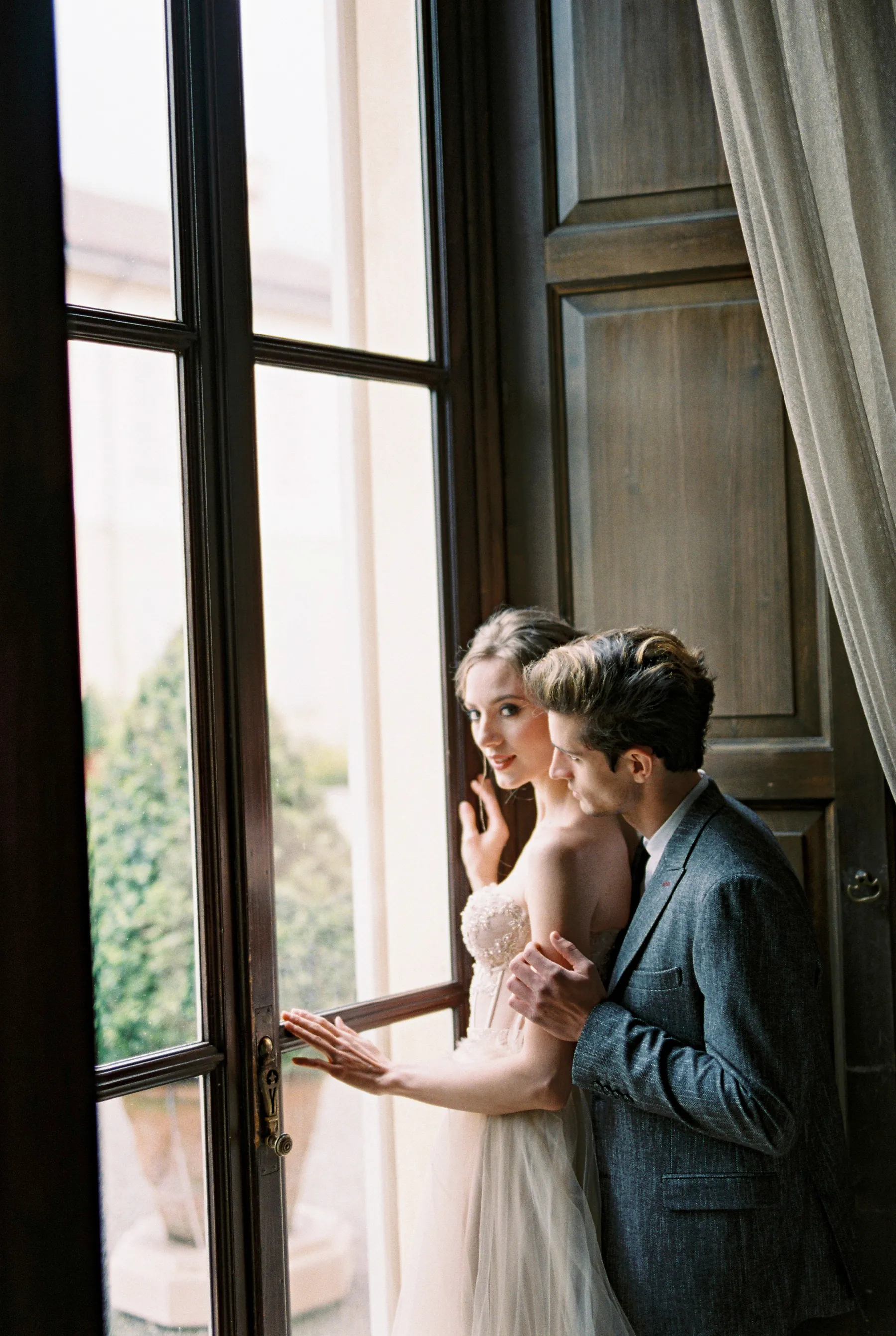 A newlywed couple embracing beside a villa window